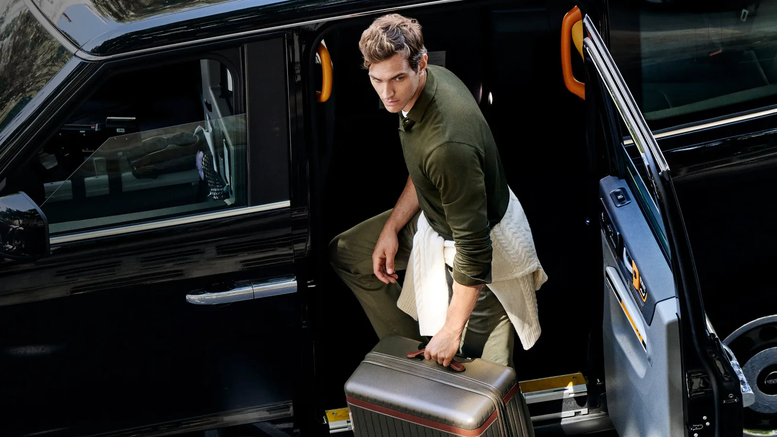 Man stepping out of a black car carrying a Carl Friedrik aluminium suitcase