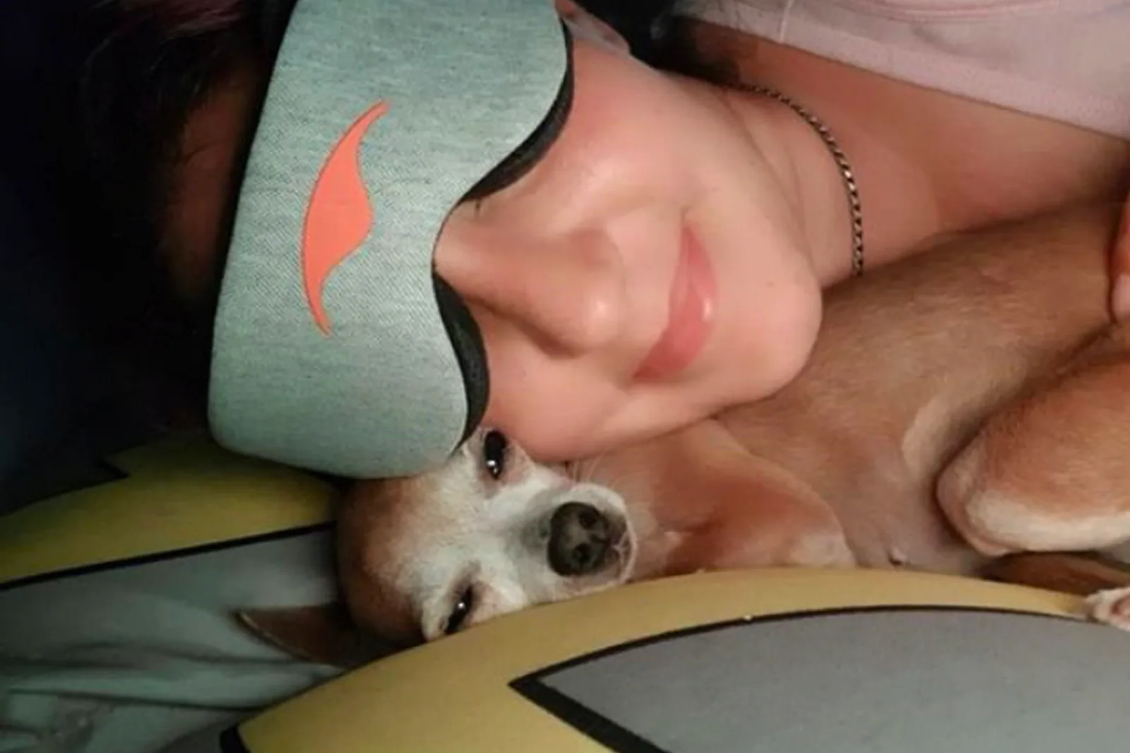 Woman in a grey Manta sleep mask lying beside a small dog